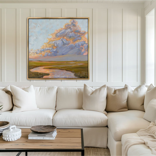 "Square Charleston marsh painting 'Thunderclouds Over the Marsh' in a gold frame, featuring lavender and periwinkle clouds styled above a neutral sofa in a bright coastal living room.