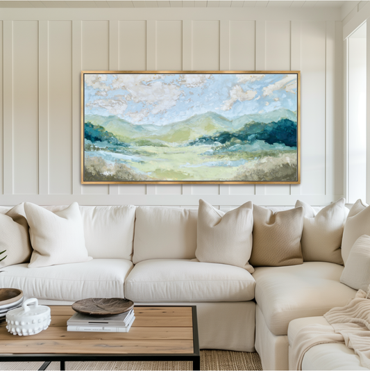 Panoramic Blue Ridge Mountain oil painting in a gold frame mounted above a white sofa.