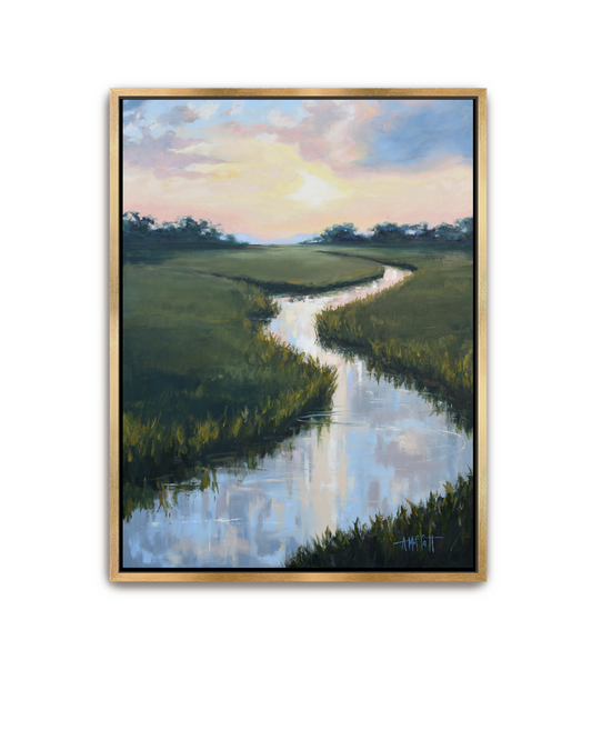 A framed landscape painting featuring a winding river reflecting a sunset sky, bordered by green marshlands, set in a light wood frame against a white background.