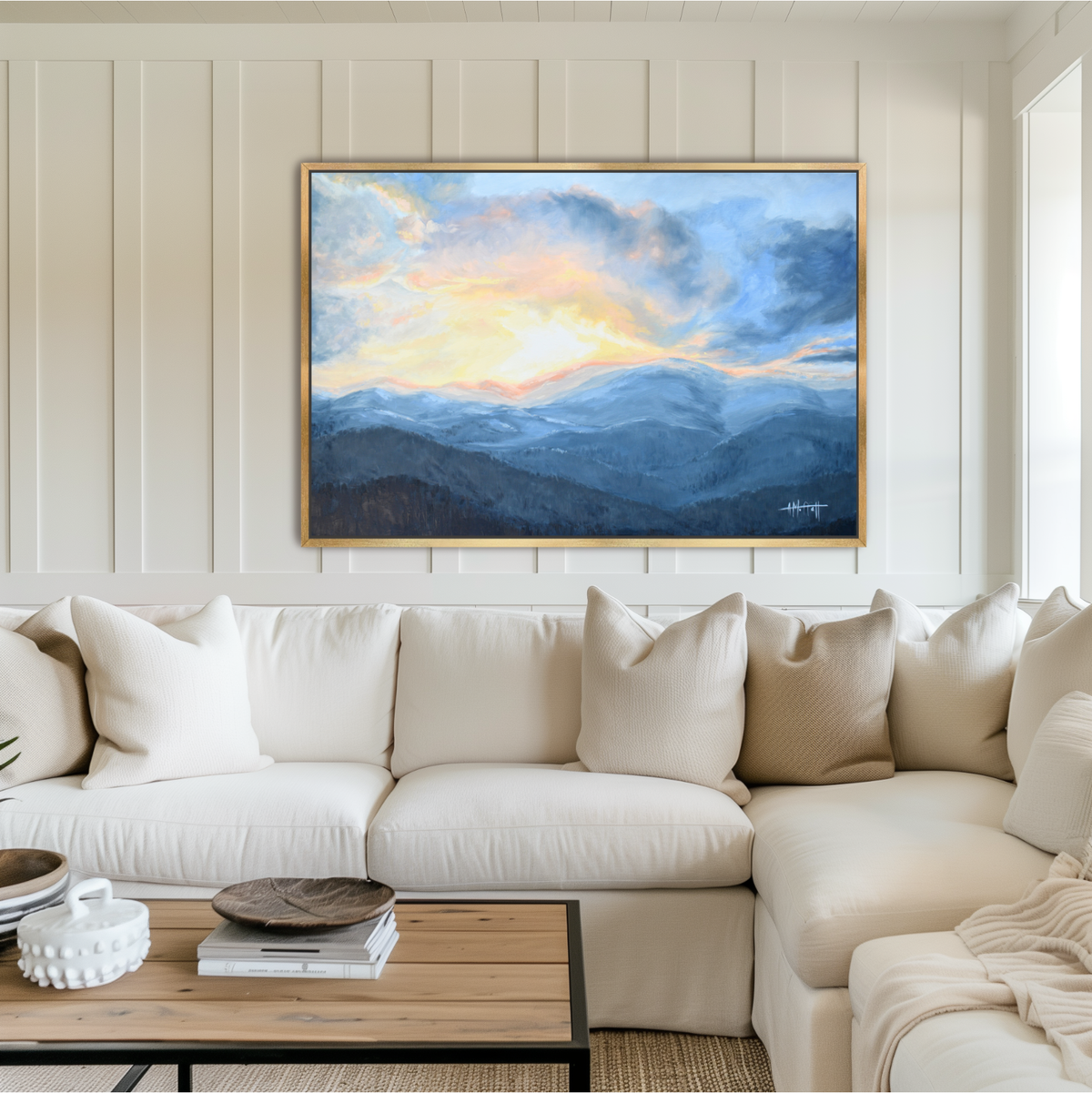 Large horizontal Blue Ridge Mountains canvas art print in a gold frame hanging above a neutral cream sofa in a coastal living room.